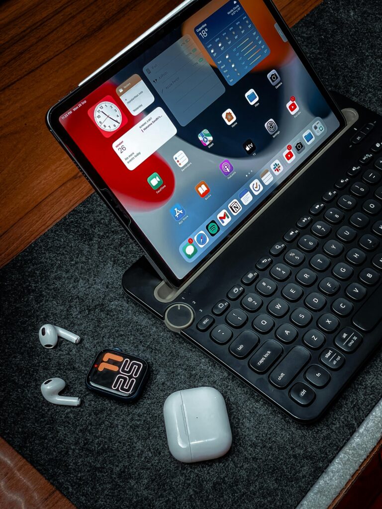 Digital workspace featuring a tablet, wireless earbuds, and a digital watch on a wooden desk.